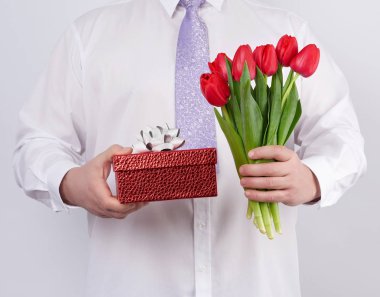 man in a white shirt and a lilac tie holding a bouquet of red tu