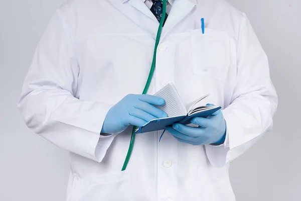 Lekarz w białym płaszczu i niebieskich rękawiczkach posiada niebieski papier notebo — Zdjęcie stockowe