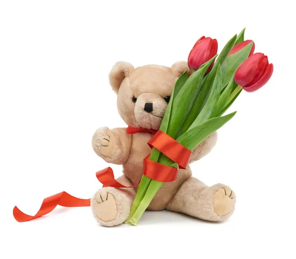 Lindo oso de peluche marrón sostiene en su pata un ramo de tulipanes rojos — Foto de Stock