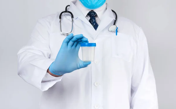 Doctor masculino con una capa blanca y corbata se para y sostiene una c de plástico —  Fotos de Stock