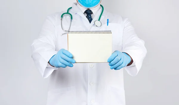 Doctor masculino con una bata blanca y guantes azules médicos sostiene una nota — Foto de Stock