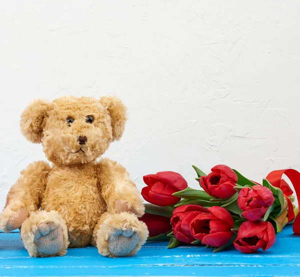 Schattige bruine teddybeer zit op een blauwe houten achtergrond en bouqu — Stockfoto