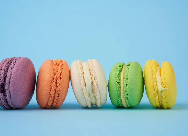 multi-colored round baked macarons cakes on a light blue background, dessert stands in a row, close up