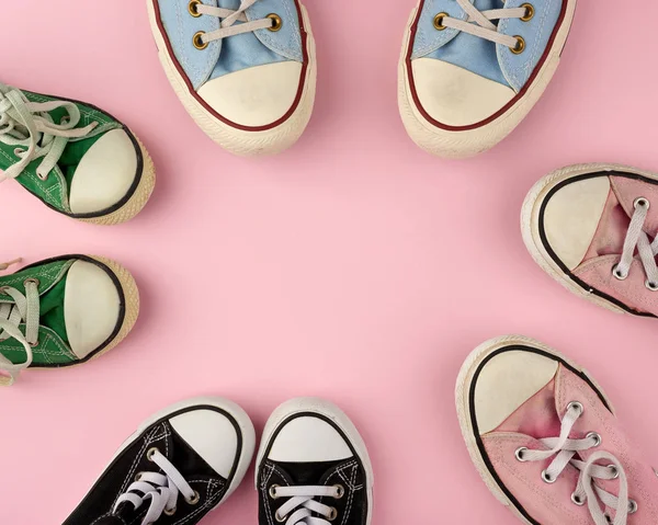 many multi-colored well-worn textile sneakers of different sizes on a pink background, top view, concept, family and team, friendship, copy space