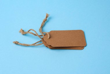 Beyaz iplikle bağlanmış boş kahverengi kağıt etiketler. Fiyat etiketi, hediye etiketi, mavi arka planda indirim etiketi, kapat