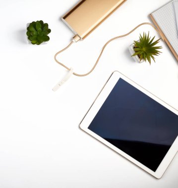 Beyaz elektronik tablet, boş siyah ekran, yeşil bitkilerin yanında beyaz masa, üst görünüm, tasarım işyeri