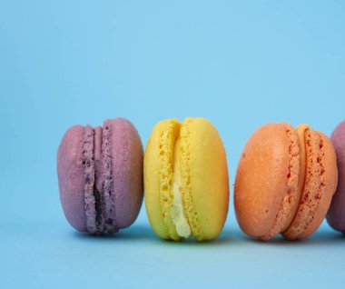 Açık mavi arkaplanda çok renkli yuvarlak badem kurabiyeleri, tatlı tezgahları üst üste, kapat.