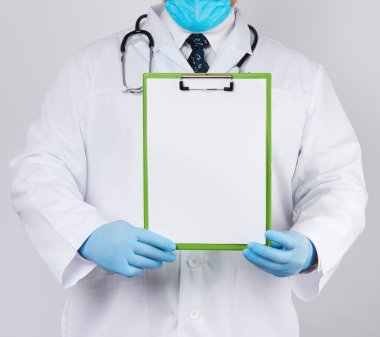 Beyaz tıbbi önlüklü ve mavi lateks eldivenli erkek doktor beyaz boş bir çarşaf ile ataç içeren bir tablet tutuyor.