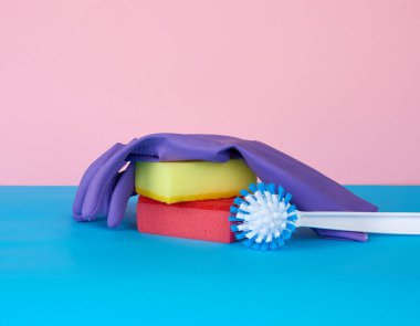 çok renkli mutfak süngeri, beyaz plastik fırça, mavi arka planda kauçuk mor eldivenler, temizlik için eşyalar.