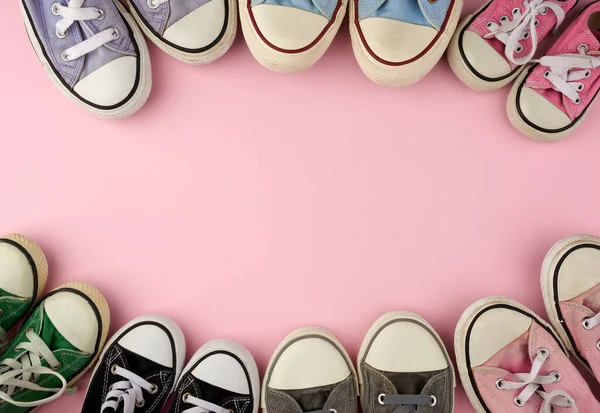 many multi-colored well-worn textile sneakers of different sizes on a pink background, top view, concept, family and team, friendship, copy space