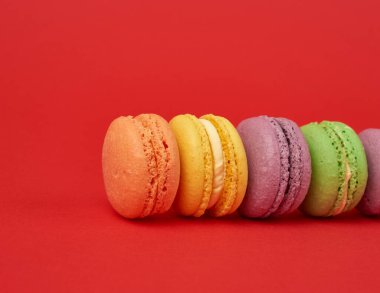 Kırmızı arkaplanda çok renkli badem unlu kurabiye yığını.