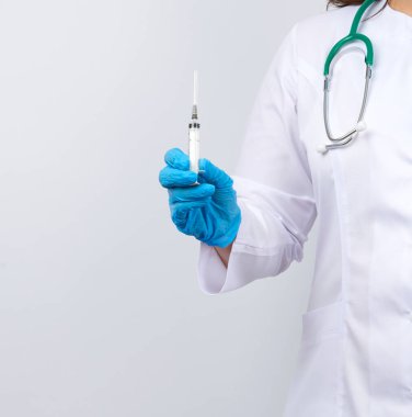 Beyaz önlüklü ve mavi lateks eldivenli sağlıkçı kadın şırınga taşıyor, beyaz stüdyo arka planı, virüslere karşı zamanında aşı kavramı