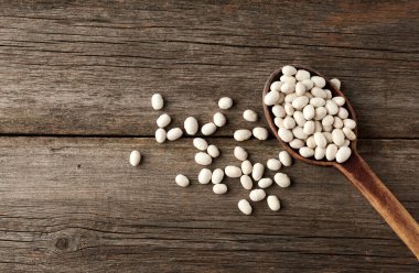 Masanın üstünde kahverengi bir kaşık içinde beyaz, çiğ fasulye.