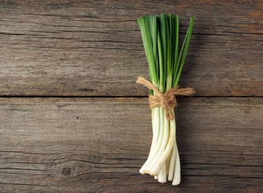 Taze yeşil soğan yaprakları, iple bağlanmış gri ahşap arka planda, üst manzara.
