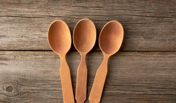 three empty brown wooden spoons on a gray wooden surface from old boards, top view