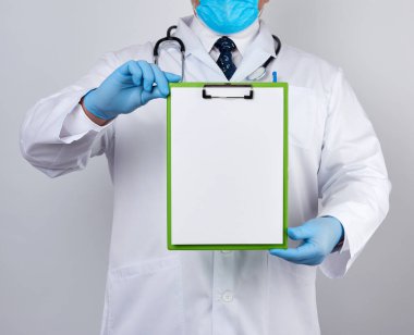 Beyaz tıbbi önlüklü ve mavi lateks eldivenli erkek doktor beyaz boş bir çarşaf ile ataç içeren bir tablet tutuyor.