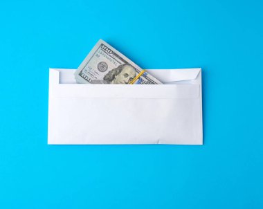 Bir paket kağıt Amerikan 100 dolarlık banknotlar elastik bir bantla bağlanmış ve beyaz bir zarfın içinde, mavi arka planda, rüşvet ve yatırım konseptinde yatıyor.