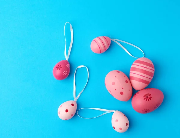 colored pink easter eggs on a blue background, close up, flat lay