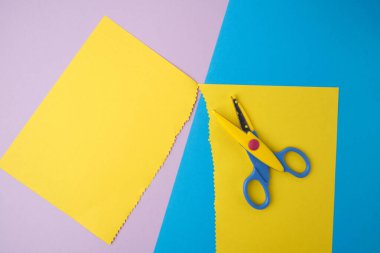 Renkli kağıdın soyut arkaplanı, zikzak uçlu sarı çizgiler ve plastik makas, üst görünüm