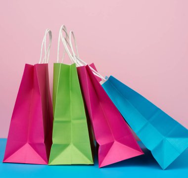 Alışveriş için çok renkli kese kağıtları ve beyaz saplı hediyeler pembe-mavi arka planda duruyor.