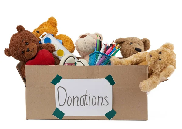 Yumuşak oyuncaklarla dolu kahverengi karton kutu, beyaz arka planda izole edilmiş okul malzemeleri, hayırseverlik kavramı ve muhtaç çocuklara yardım