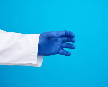  El, mavi steril lastik eldiven takıyor. Elinde bir nesne var. Mavi arka plan.