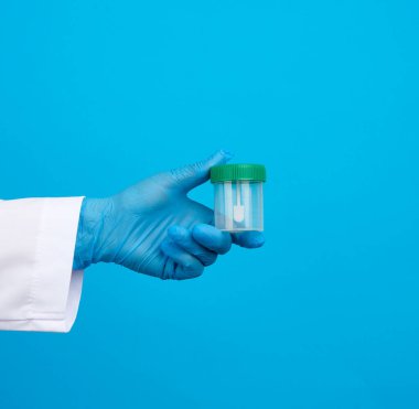 Beyaz önlüklü ve mavi steril lateks eldivenli doktor dışkı analizi için plastik bir kavanoz tutuyor.