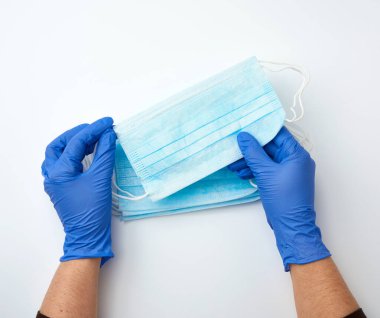 Eller, beyaz arka planda virüslere ve bakterilere karşı tıbbi bir maske tutuyor. Koruyucu tıbbi araç, üst görünüm.