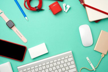 Klavye, kablolu altın güç bankası, boş siyah ekranlı kırmızı akıllı telefon, kulaklıklar, boş kağıt kartvizitler ve yeşil arka planda kablosuz fare, işyeri, üst görünüm