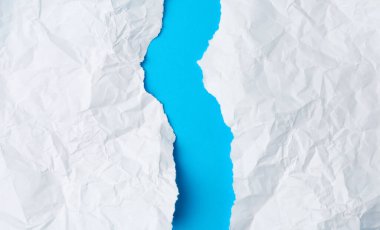Kırışmış beyaz kağıt parçası mavi arka planda ikiye bölünmüş. Kağıt parçası yırtılmış kenar.