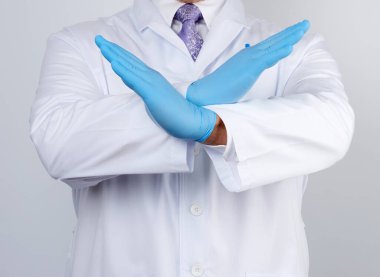 Beyaz önlüklü ve mavi lateks eldivenli doktor kollarını göğsünün önünde kavuşturdu. Reddetme hareketi, inkar etme.