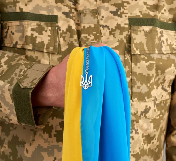 Ukraynalı bir savaşçı askeri piksel üniforması içinde Ukrayna eyaletinin sarı-mavi bayrağını taşıyor ve zincirin üzerinde mızrak ülkesinin küçük bir arması var.