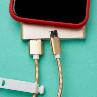 Beyaz ekranlı kırmızı akıllı telefon bir elektrik kablosu ile bağlanır, yeşil arkaplan, üst görünüm