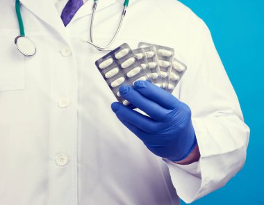 Mavi steril eldivenli erkek eli su toplayan bir ilaç yığını, hastalıkların tedavi konsepti, mavi arka plan