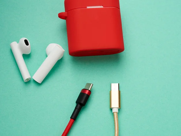 red charging box and sticks headphones on a green background, close up
