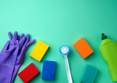 temizlik için mor lastik eldiven, çok renkli sünger, fırça ve temizlik sıvısı yeşil bir plastik şişede yeşil arka planda, mesaj için yer, düz uzanma