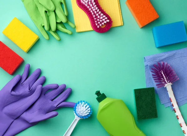 rubber gloves for cleaning, multi-colored sponges, brushes and cleaning fluid in a green plastic bottle on a green background, place for text, flat lay