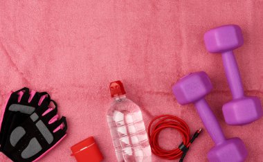 Bir çift mor plastik dambıl, kulaklık, ve pembe terry havlu, üst görüş, eğitim ekipmanı