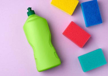 çok renkli mutfak dikdörtgen bulaşık süngeri ve yeşil plastik şişe deterjan, mor arka plan