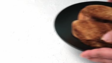 Beyaz buğday unundan yapılmış iki dilim kızarmış ekmek siyah yuvarlak bir tabakta, eller beyaz arka plana yemek koyuyor.