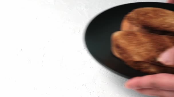 白面粉做成的两片油炸面包装在一个黑色圆盘里 用手把食物放在白色的背景上 — 图库视频影像