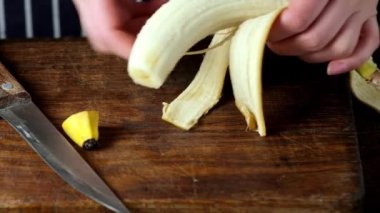 Kadın eli, kahverengi bir kesme tahtasının üzerinde taze sarı bir muzu soyar ve keser.