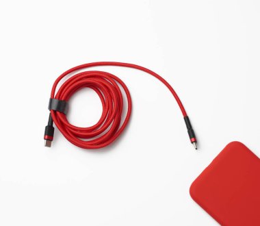 Beyaz arka planda tekstil örgülü kırmızı akıllı telefon ve kablo, yakın plan, düz yat