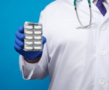 Mavi steril eldivenli erkek eli su toplayan bir ilaç yığını, hastalıkların tedavi konsepti, mavi arka plan