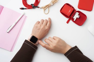 Siyah ekranlı akıllı saat sol elinde, sağ eli saat ekranına dokunuyor, serbest çalışan işyeri açık bir defter, üst görünüm, evde çalışıyor.