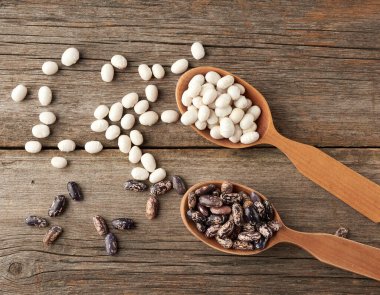 Oval ve yuvarlak kahverengi ve beyaz fasulyeler tahta bir kaşıkta gri bir arka planda, üst manzara