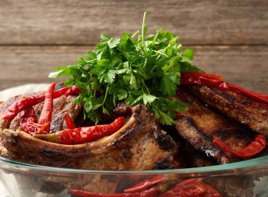 Kemiğin üzerinde ızgara domuz bifteği şeffaf bir cam tabakta, ahşap bir masada, barbekü