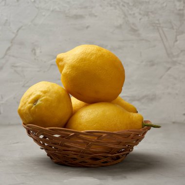 Gri bir masada hasır sepetteki olgun sarı limonlar, limonata malzemesi.