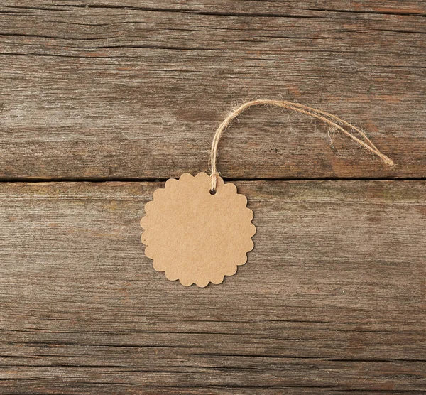 Round empty brown paper tag tied with white string. Price tag, gift tag, sale tag on the gray wooden background, close up