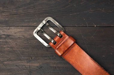Kahverengi deri erkek kemeri, ahşap bir arka planda metal toka, üst manzara.